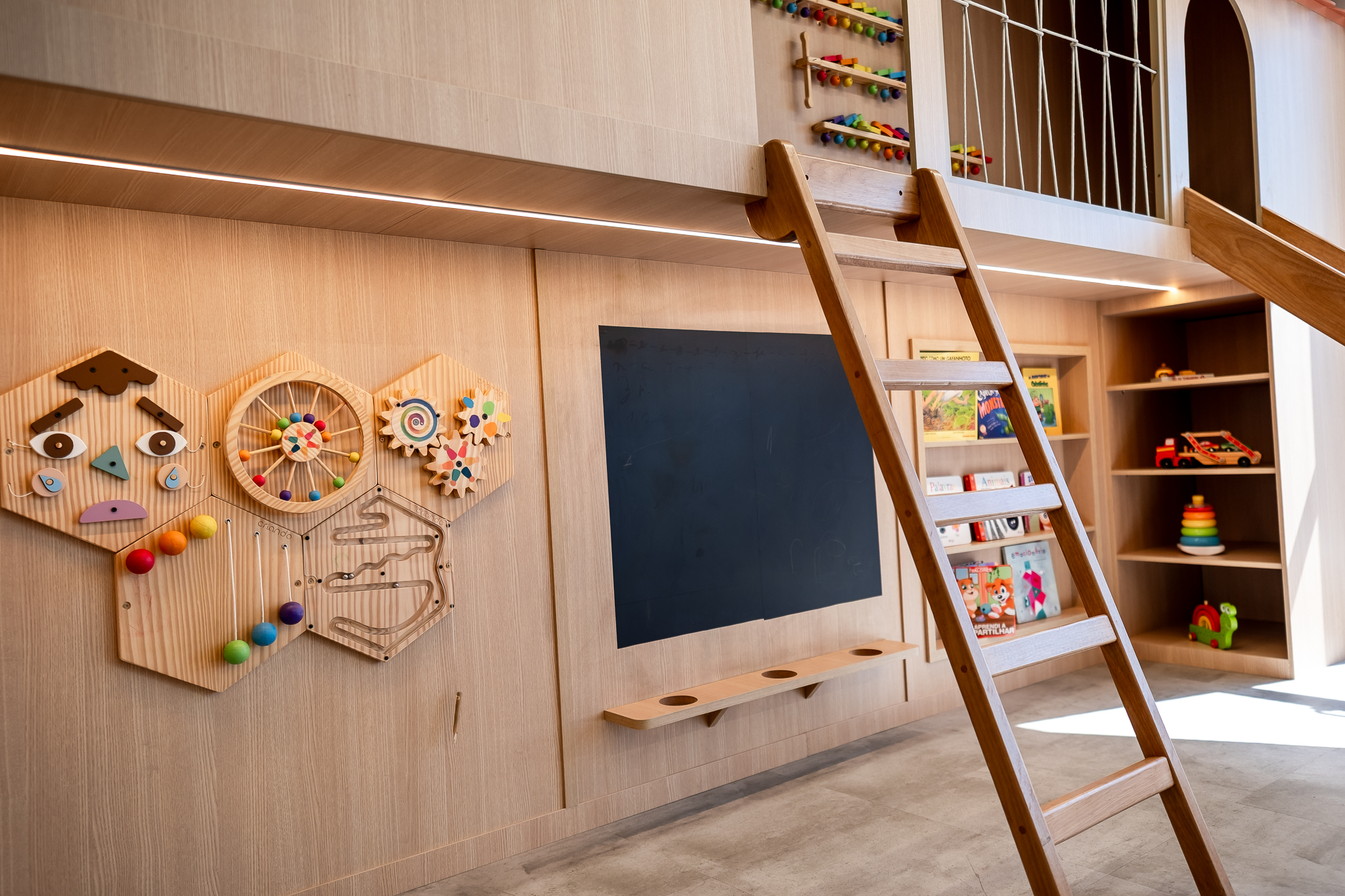 Detalhe da parede de brinquedos sensoriais e estante de livros infantis