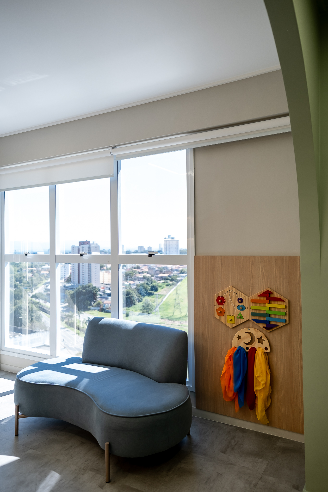 Sala de espera com chaise e parede de estímulos sensoriais, vista da cidade ao fundo